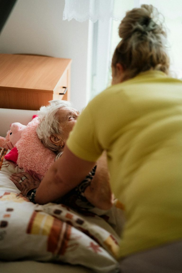 Nurse assisting elderly woman in a comfortable medical facility setting.